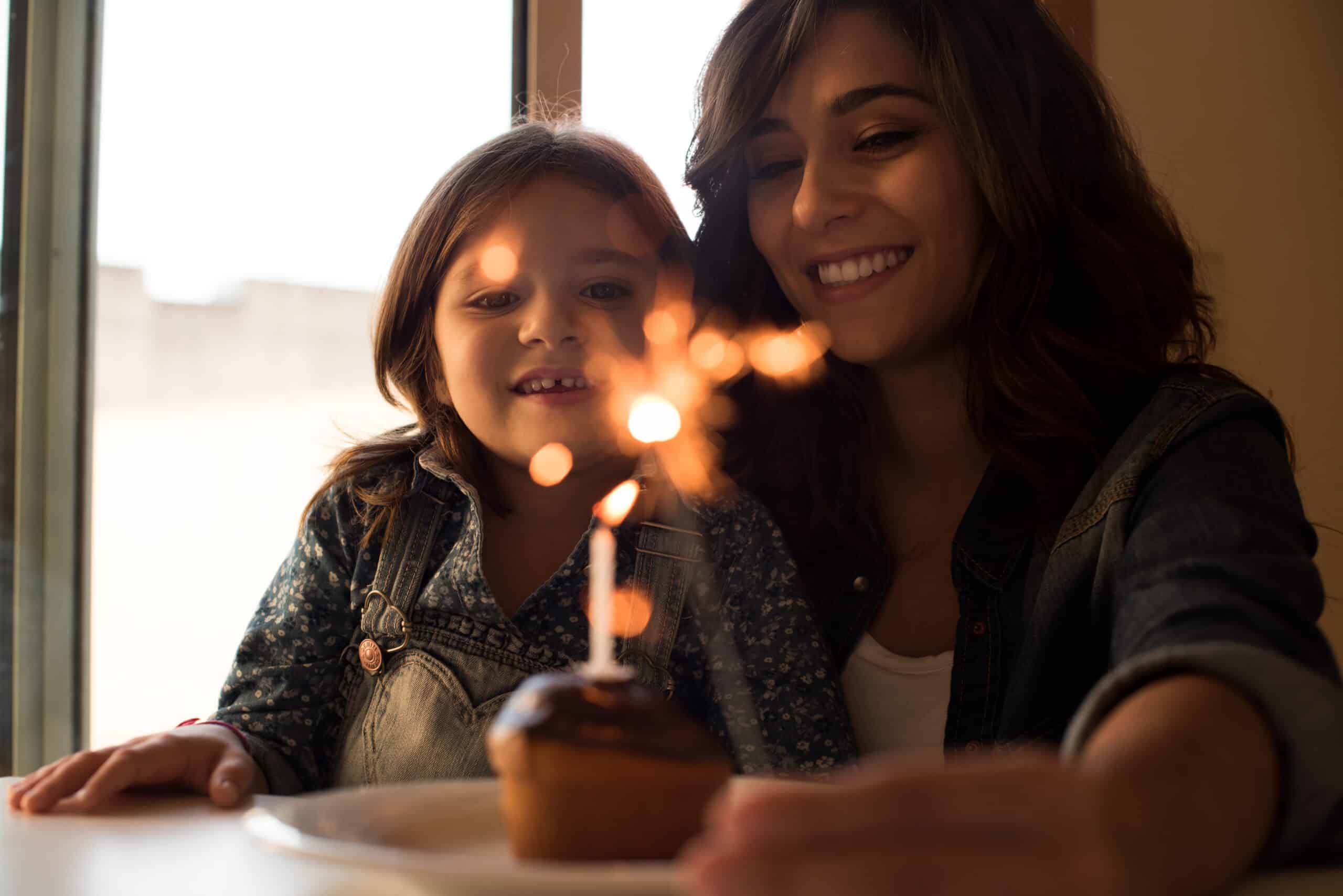 A mother and daughter with a birthday cupcake and sparkler